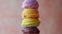 Colorful macarons stacked in tower with purple, yellow, green and chocolate flavors on soft pink background for dessert menu design.