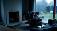 Young Caucasian mother and child reading together in a cozy armchair by fireplace on a rainy day, warm family moment at home.