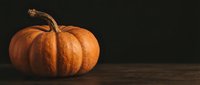 Orange pumpkin with curved stem on rustic wooden surface against dark background for autumn harvest decorations and seasonal holiday designs.
