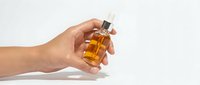 Hand holding amber glass dropper bottle with golden serum or essential oil against white background for skincare and beauty product mockup.