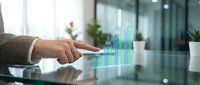 Businessman pointing at holographic bar chart with growth data on digital tablet in modern office workspace with plants.