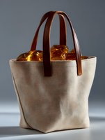 Stylish canvas tote bag with brown leather handles filled with glowing amber stones against gray background, dramatic lighting creates mystical atmosphere.