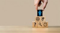 Hand placing wooden cube with blue human figure icon on stack of blocks featuring AI and business symbols on neutral background.