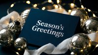 Seasons Greetings card in navy blue with silver text, surrounded by gold ornaments and warm fairy lights for holiday greeting designs.