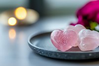 Rose quartz crystal hearts on dark plate with candles and flowers creating romantic spa wellness atmosphere for meditation and healing rituals.
