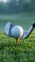 Golf club iron positioned behind white ball on wooden tee sitting on green grass course with blurred background for sports and recreation concepts.