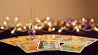 Mystical pendulum swinging over colorful tarot cards with warm bokeh lights creating magical fortune telling atmosphere for spiritual guidance sessions.