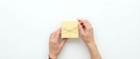 Hands holding a small yellow gift box with ribbon on white background, top view. Holiday present concept for greeting cards and banners.