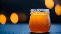Fresh honey in glass jar with crystallized rim against blurred warm bokeh lights, showcasing natural sweetener on dark background with golden glow.