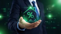 Businessman holding glowing green house with percentage symbol representing mortgage rates, real estate investment and property financing concepts.