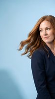 Confident redhead woman in navy blue top with flowing hair against light blue background, professional portrait for business and lifestyle content.