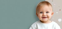 Smiling baby with blue eyes wearing white shirt against dual-colored background with decorative dots, perfect for parenting blogs and childcare advertisements.