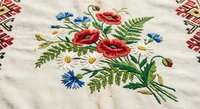 Traditional folk embroidery with red poppies, white daisies, blue cornflowers and green ferns on natural linen fabric with decorative border pattern.