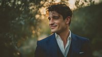 Handsome young Caucasian businessman in navy blue suit smiling outdoors during golden hour sunset with natural bokeh background for corporate headshots.
