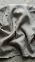 Natural linen fabric with soft folds and wrinkles creating organic texture and shadows on neutral stone surface for home decor and textile design projects.