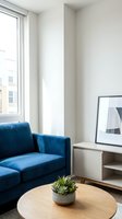 Modern living room corner with blue velvet sofa, round wooden table, potted succulent, framed artwork on white shelving unit, and bright window light for contemporary home decor.