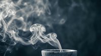 White smoke swirls rising from cup creating elegant flowing patterns against dark background for aromatherapy and relaxation concepts.