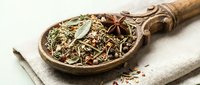 Aromatic herbal tea blend with star anise and dried herbs in rustic wooden spoon on natural linen fabric for wellness and culinary applications.