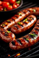 Grilled sausages with herbs cooking on barbecue grill with fresh tomatoes in background for summer outdoor dining and cookout celebrations.