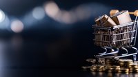 Mini shopping cart filled with tiny gift boxes standing on golden coins against dark background with bokeh lights, concept of consumer spending.