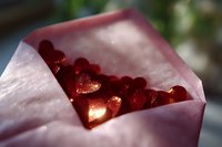 Red glittering hearts scattered in pink paper envelope creating romantic atmosphere with soft bokeh background, suitable for Valentine's day designs and love concepts.