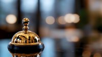 Golden hotel service bell on reception desk with blurred lobby background for hospitality and customer service concepts.