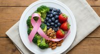 Pink ribbon with healthy foods broccoli blueberries strawberries nuts on white plate for breast cancer awareness nutrition support wooden background.