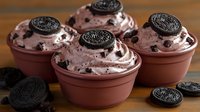 Creamy cookies and cream dessert cups topped with chocolate sandwich cookies and whipped cream swirls on wooden surface, sweet treat for parties and celebrations.