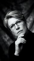 Thoughtful middle-aged man with light hair wearing eyeglasses and dark clothing, hand near face in contemplative pose against blurred background. Portrait photography.