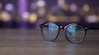 Stylish eyeglasses with reflective lenses on wooden surface against blurred city lights background for vision care and fashion concepts.