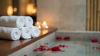 Luxury spa bathtub with rolled white towels and scattered red rose petals creating romantic wellness atmosphere for relaxation and self-care rituals.