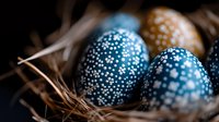 Decorative Easter eggs painted in deep blue with delicate white dot patterns nestled in natural straw nest. Traditional holiday celebration background.