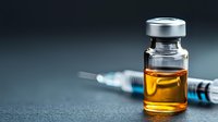 Medical vial with amber liquid and syringe on dark background, dramatic lighting creates scientific atmosphere for healthcare and pharmaceutical concepts.