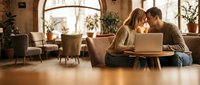 Young couple working together on laptop in cozy modern living room with warm lighting and plants creating intimate home office atmosphere.
