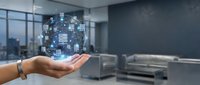 Hand holding a glowing digital network globe with connected nodes, representing cloud computing and data management in a modern office setting.