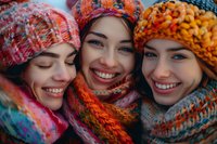 Three young diverse women wearing colorful knitted winter hats and scarves smiling together in close-up portrait, perfect for seasonal fashion, friendship and lifestyle advertising.