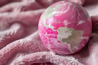 Colorful bath bomb with pink and white swirled pattern on soft pink towel, ready to dissolve in water for aromatherapy spa experience.