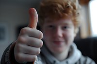 Young blonde man giving thumbs up gesture with positive expression and casual hoodie clothing in indoor setting for success and approval concepts.