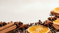 Aromatic winter spices with dried orange slices, cinnamon sticks, star anise and coffee beans arranged on neutral background for seasonal cooking and baking.
