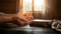 Mature hands cupping glowing light bulb on wooden table with open book and rope, symbolizing ideas, knowledge, and spiritual enlightenment for educational and inspirational projects.