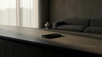 Modern minimalist workspace with dark countertop, smartphone, and gray sofa in contemporary interior design setting for home office or studio projects.