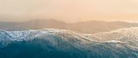 Aerial view of turquoise ocean waves meeting sandy beach shore at sunset with warm golden light creating peaceful coastal scenery for travel and vacation themes.