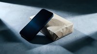 Smartphone leaning against kraft paper box on concrete surface with dramatic shadow, suitable for tech product mockups and packaging design concepts.