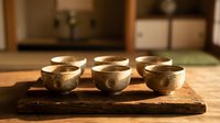 Six handcrafted ceramic tea cups arranged on rustic wooden tray in warm kitchen setting. Traditional pottery bowls perfect for tea ceremony or dining decor.