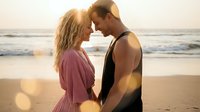 Romantic couple embracing on beach at golden hour sunset with ocean waves. Young Caucasian man and woman sharing intimate moment during vacation getaway.
