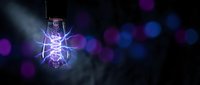 Glowing vintage Edison bulb with electric filament against dark background with colorful bokeh lights creating atmospheric lighting effect.