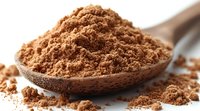 Ground cocoa powder in wooden spoon, close up view on white background. Fine brown chocolate dust scattered around showing texture and detail.