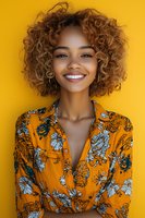 Happy young African American woman with curly hair smiling against bright yellow background wearing floral orange shirt for lifestyle content.