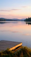 Serene lake at sunset with wooden dock and mountain silhouettes reflecting in calm water creating peaceful evening atmosphere for relaxation and nature themes.