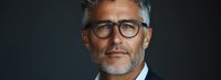 Confident mature businessman with gray hair and stylish glasses against dark background, professional corporate portrait showing experience and leadership.